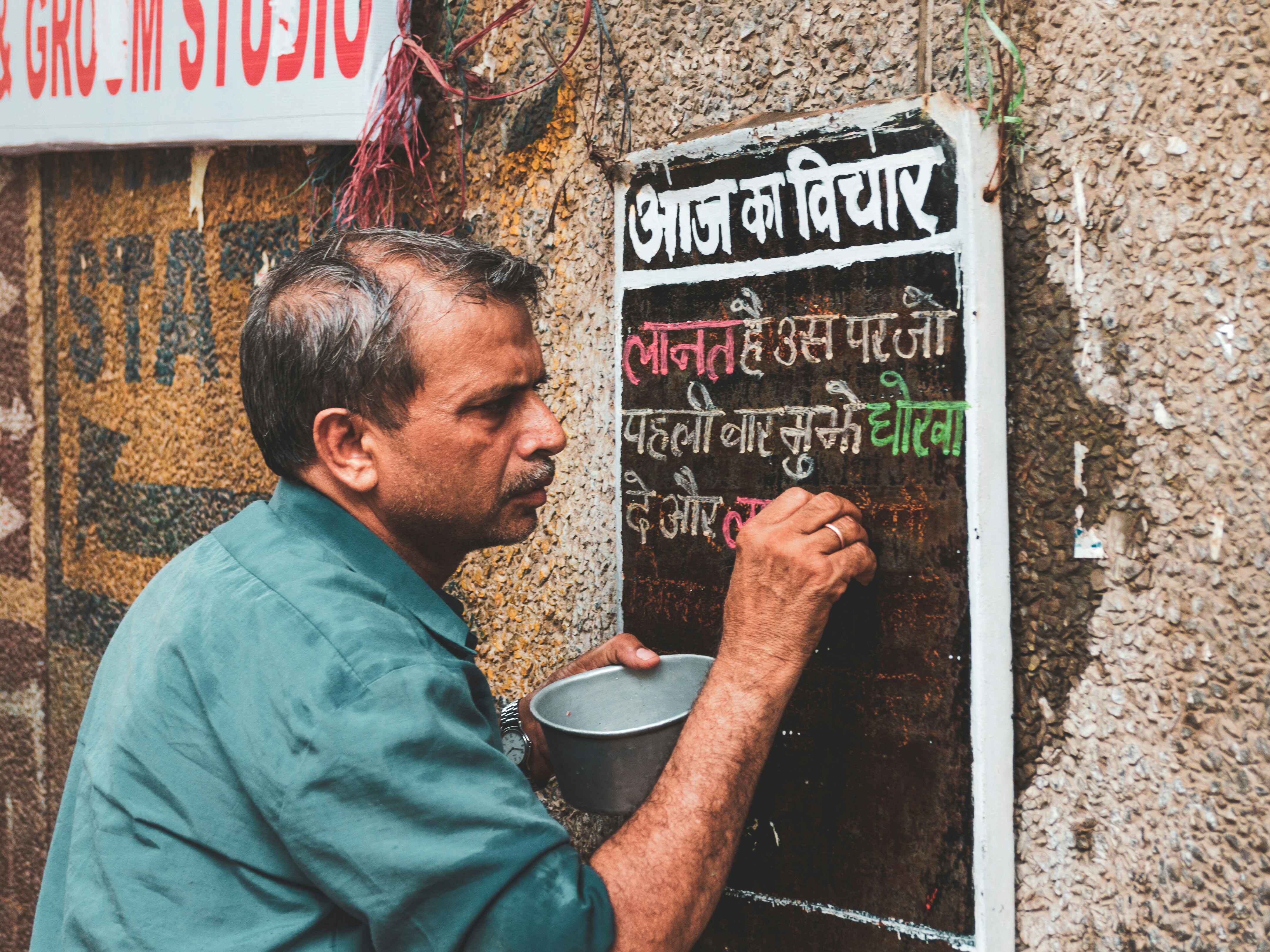 a man painting the wall In hindi text; Credit: @Akshat Vats on Unsplash